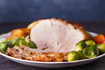 Roasted sliced ham and vegetables: potatoes, carrots, brussel sprouts, cabbage and green peas on black wooden background. copy space