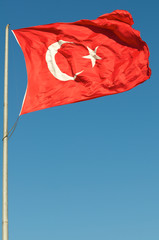 Bright red silken flag of Turkey fluttering in the wind against clear blue sky