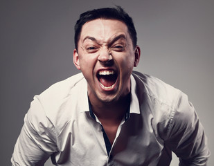 Angry business man strong and loud screaming with wide open mouth on grey background. Closeup