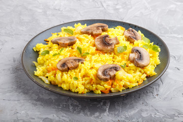 Yellow fried rice with champignons mushrooms, turmeric and oregano on blue ceramic plate on a gray concrete background. side view.