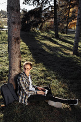 Young male student in casual outfit using notebook or laptop while sitting on the grass at the park.