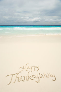 Tropical Happy Thanksgiving travel message handwritten in calligraphy on smooth sand beach