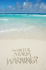 Cheeky Winter Storm Warning? message handwritten on tropical beach to make the friends at home envious