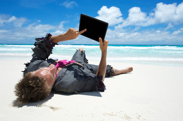 Castaway businessman relaxing with wifi on a tropical beach using his tablet computer