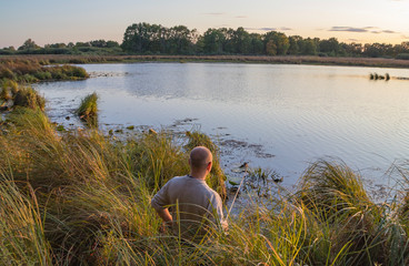 A fisherman catches fish on the shore of the pond at dawn.