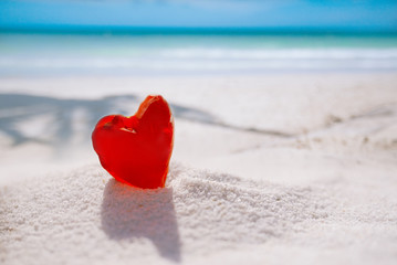 red heart shaped sea glass on white sand beach