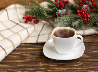 Black tea in a white cup with a saucer on a wooden table, spruce branch and light textile in the background. Winter tea