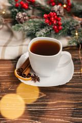 Black tea in a white cup with a saucer on a wooden table, spruce branch and light textile in the background. Winter tea