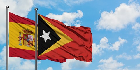 Spain and East Timor flag waving in the wind against white cloudy blue sky together. Diplomacy concept, international relations.