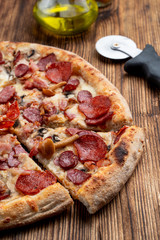 Close up of seasonal pizza with wild mushrooms and pepperoni on wooden table with ingredients on it