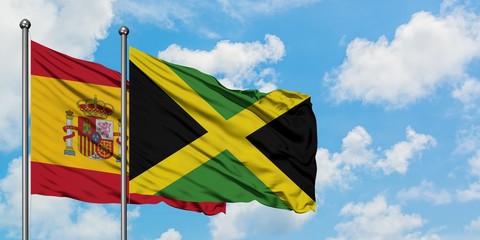 Spain and Jamaica flag waving in the wind against white cloudy blue sky together. Diplomacy concept, international relations.