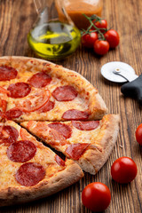 Close up of pepperoni pizza on wooden table with ingredients on it
