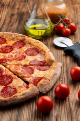 Close up of pepperoni pizza on wooden table with ingredients on it
