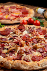 Close up of seasonal pizza with wild mushrooms and pepperoni on wooden table with ingredients on it