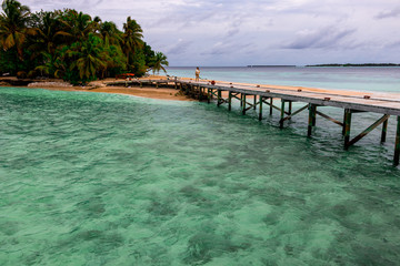 puente madera sobre mar turquesa hacia playa con palmeras