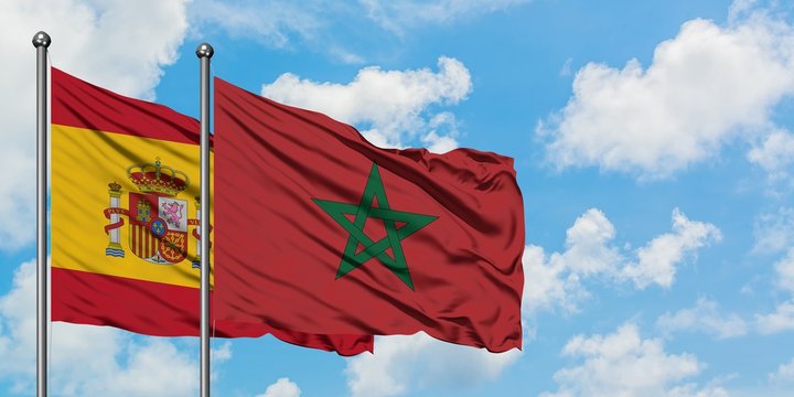 Spain and Morocco flag waving in the wind against white cloudy blue sky together. Diplomacy concept, international relations.
