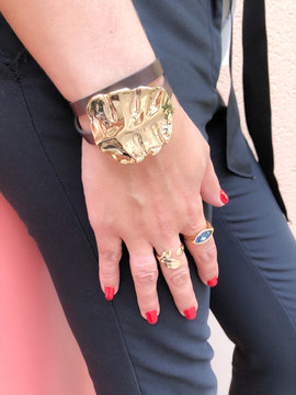 Dropped woman's hand wearing brown leather bracelet with big gold leaf decoration, golden rings, red manicure