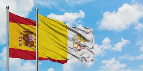 Spain and Vatican City flag waving in the wind against white cloudy blue sky together. Diplomacy concept, international relations.