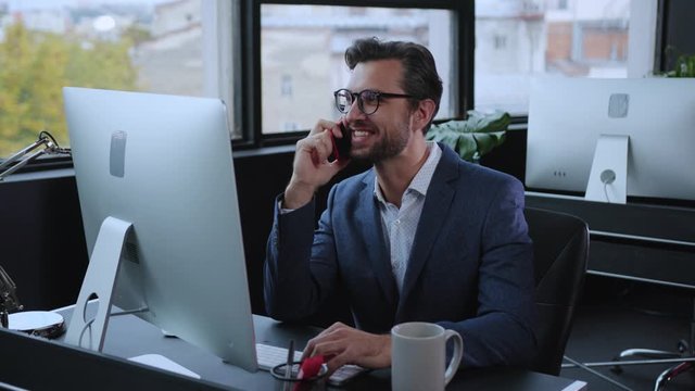 Relaxed office employee talking on phone with a girlfriend smiling laughing enjoying break time sitting at computer table in the office. Business person.