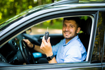 Young driver man sitting inside new car with keys. Smiling