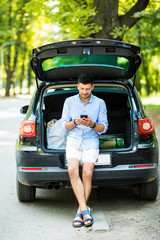 Young man sitting in his car trunk and use phone in the street road