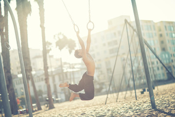 A young man athlete working out on traveling rings on muscle beach, Santa Monica, California