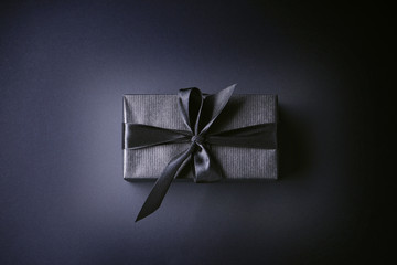 Gift in black paper with a black ribbon on a black background, flat lay. Black Friday concept. 