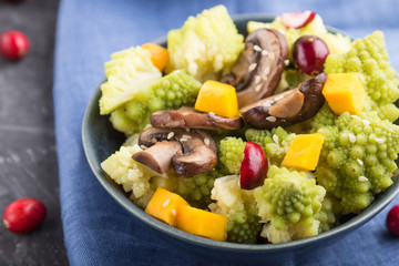 Vegetarian salad from romanesco cabbage, champignons, cranberry, avocado and pumpkin on a black concrete background. side view, selective focus.
