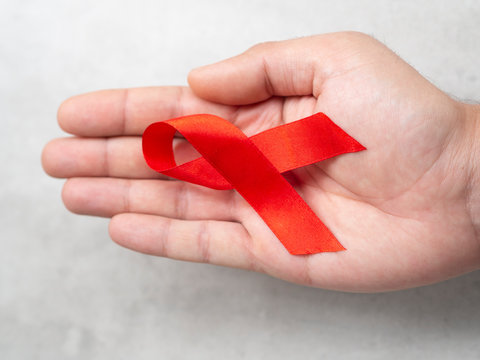 Close up top view man's hand holding a red AIDS awareness ribbon. 01 December HIV Awareness campaign concept.