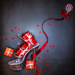 High heel shoe filled with red Christmas gifts and a polka lollipop tied to the heel with a red ribbon. Dark background.