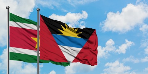 Suriname and Antigua and Barbuda flag waving in the wind against white cloudy blue sky together. Diplomacy concept, international relations.
