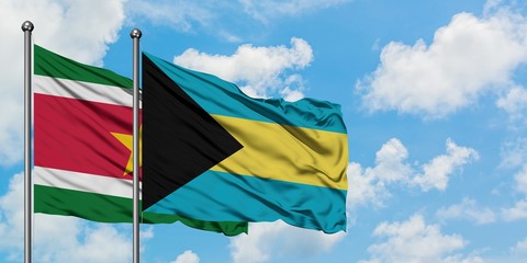 Suriname and Bahamas flag waving in the wind against white cloudy blue sky together. Diplomacy concept, international relations.