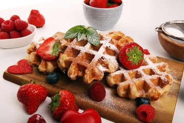 Traditional belgian waffles with fresh blueberries, sugar and raspberries on rustic table