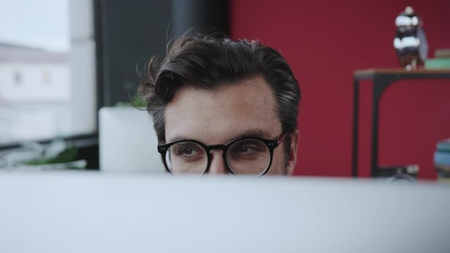 Close-up office supervisor spying his employees working hiding behind computer monitor. Funny strict businessman keeping order in the office.