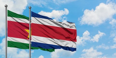 Suriname and Costa Rica flag waving in the wind against white cloudy blue sky together. Diplomacy concept, international relations.