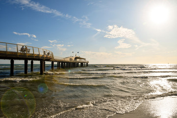Backlight view with lens flare of Pontile Bellavista Vittoria, a modern pedestrian pier on the seashore of the Versilia coast in Tuscany with people, Lido di Camaiore, Lucca province, Italy