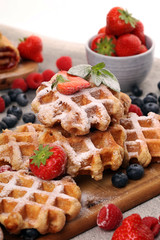 Traditional belgian waffles with fresh blueberries, sugar and raspberries on rustic table