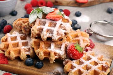 Traditional belgian waffles with fresh blueberries, sugar and raspberries on rustic table