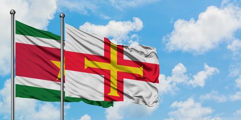 Suriname and Guernsey flag waving in the wind against white cloudy blue sky together. Diplomacy concept, international relations.