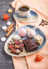 A pieces of homemade chocolate with coconut candies and a cup of coffee on a black concrete background. side view, close up.