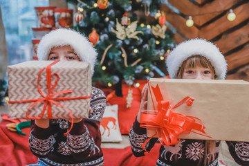 Close up photo of son and daughter who prepared Xmas gifts for their parents and are showing them to the camera, looking proud of what they've done.