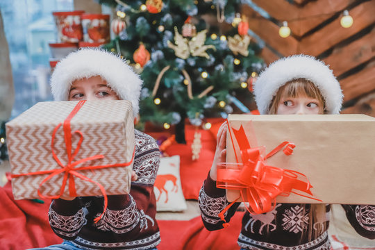Close up photo of son and daughter who prepared Xmas gifts for their parents and are showing them to the camera, looking proud of what they've done.