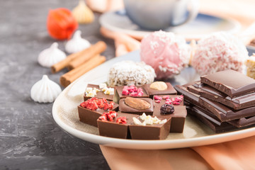 A pieces of homemade chocolate with coconut candies and a cup of coffee on a black concrete background. side view, selective focus.