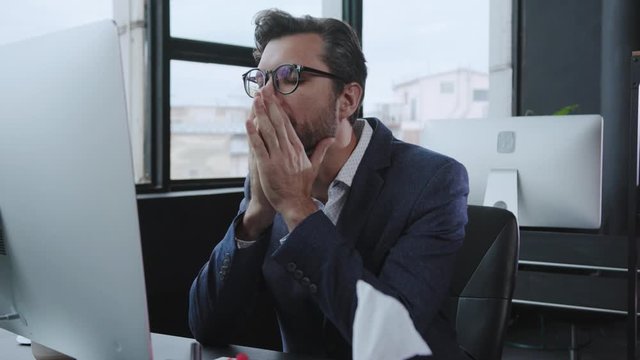 Unwell male executive coughing of fever or cold blowing his nose sneezing allergy while working at office table. Bad feeling. Healthcare concept.