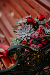 Fototapeta na wymiar Beautiful autumn bouquet with red flowers and succulents on a bench outside