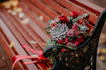 Fototapeta na wymiar Beautiful autumn bouquet with red flowers and succulents on a bench outside