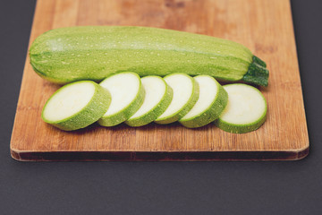 Green courgette or zucchini fresh and raw whole and sliced on the wooden cutting board on black background.