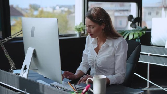 Young successful business woman working on desktop computer at office table. Confident female manager performing work tasks in contemporary company office.