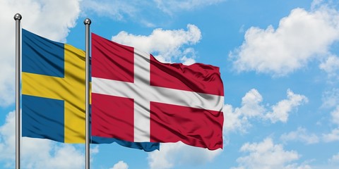 Sweden and Denmark flag waving in the wind against white cloudy blue sky together. Diplomacy concept, international relations.
