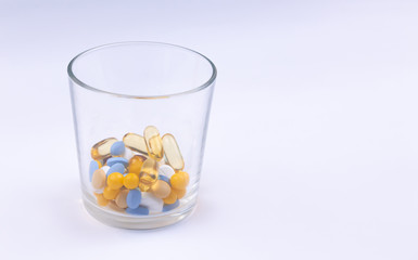 Dose of the colored pills in the glass of the package of pills. On white background with copy space...